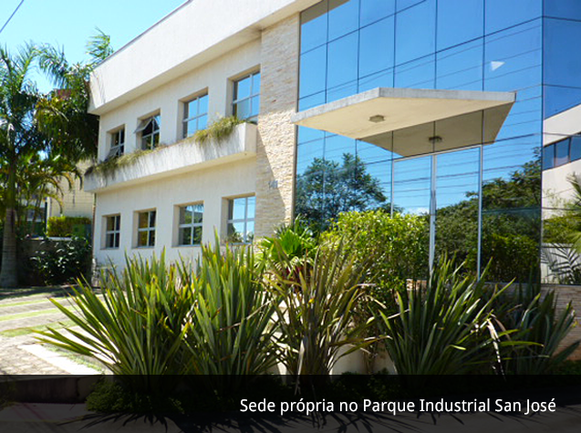 Sede própria no Parque Industrial San José. Fachada de vidro, janelas e plantas no jardim.